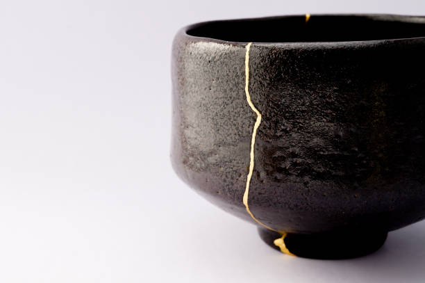 Antique broken Japanese raku black bowl repaired with gold kintsugi technique stock photo