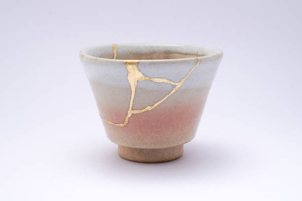 Antique broken Japanese beige sake cup repaired with gold kintsugi technique stock photo