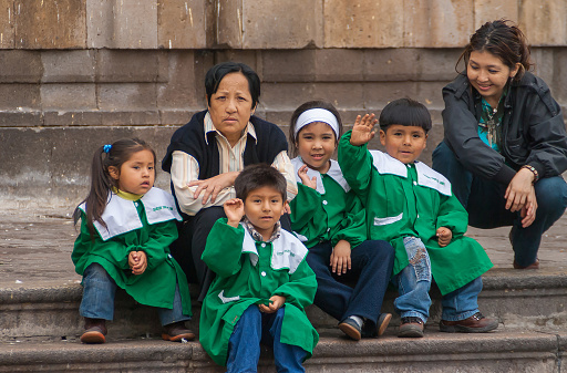 Lima, Peru - December 4, 2008: Closeup of Group of small children dressed in green sit with teachers on steps of Sanctuary of our lady of Solitude yellow facade church.