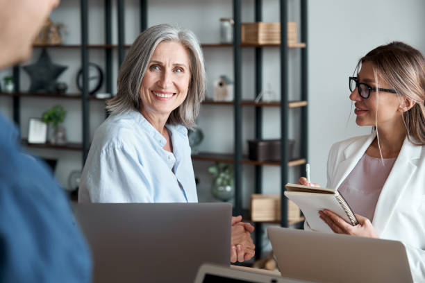 istock Smiling mature old female mentor coach manager training young interns at group office meeting workshop. Happy middle aged teacher working together with students at classÂ  seminar. Mentoring concept. 1280371006