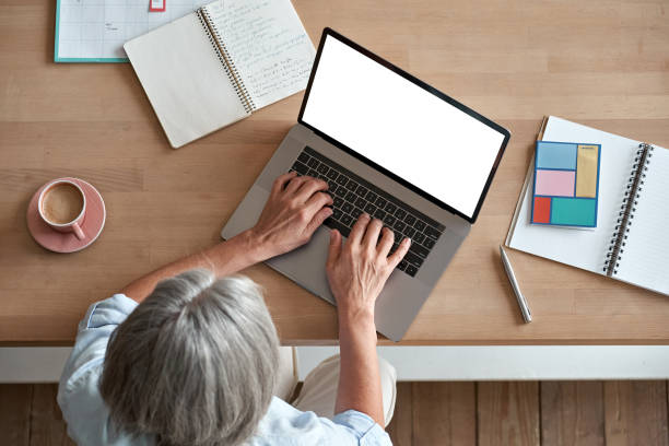 istock Mature middle aged business woman using laptop computer sitting at workplace desk. Senior older lady, 60s grey-haired businesswoman working at table typing on pc at home or from office, top view. 1280371022