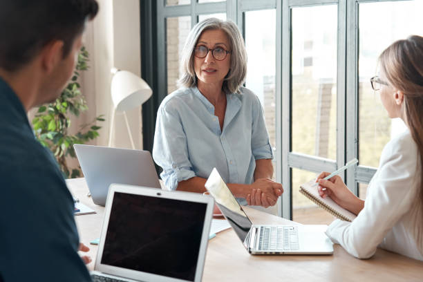 istock Mature old female mentor coach supervisor training young interns at group office meeting professional workshop. Middle aged business woman teacher professor working with students at university class. 1280371023