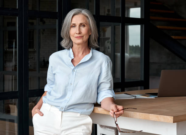 confident stylish european mature middle aged woman standing at workplace. stylish older senior businesswoman, 60s gray-haired lady executive leader manager looking at camera in office, portrait. - business woman imagens e fotografias de stock