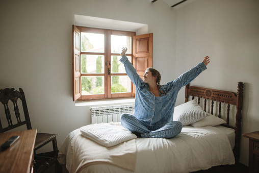 A young woman wearing pajamas stretching in a bed