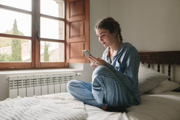 istock Young woman sitting on bed using her smart phone 1280373161