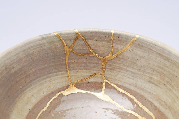 Antique broken Japanese beige bowl repaired with gold kintsugi technique stock photo