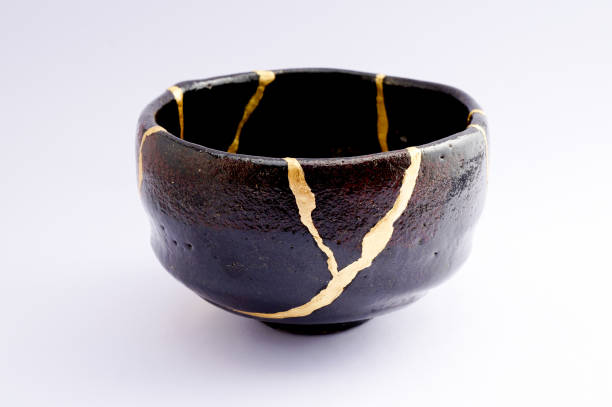 Antique broken Japanese black raku bowl repaired with gold kintsugi technique stock photo