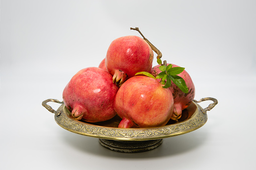 Pomegranates on a brass fruit bowl on a white background