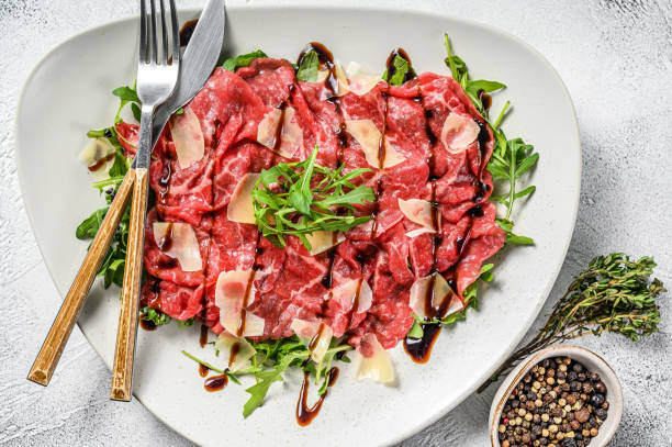 Italian Beef carpaccio with arugula salad, parmesan cheese. Gray background. Top view Italian Beef carpaccio with arugula salad, parmesan cheese. Gray background. Top view. carpaccio parmesan cheese beef raw stock pictures, royalty-free photos & images