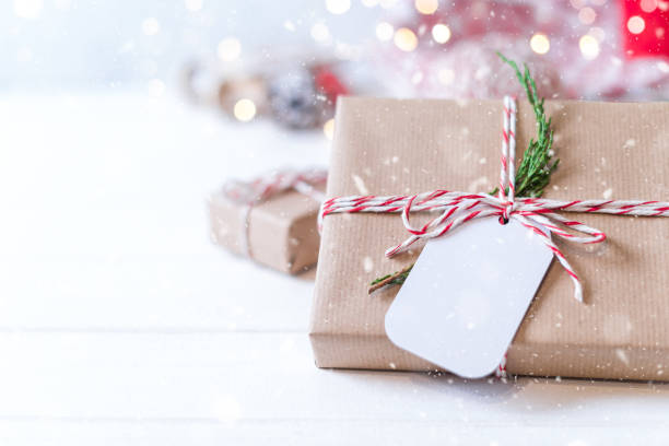 istock Christmas eco gift with empty tag. Glowing snow bokeh, coniferous branch. Winter holidays mock up on white background. Zero waste, plastic free. 1280377294