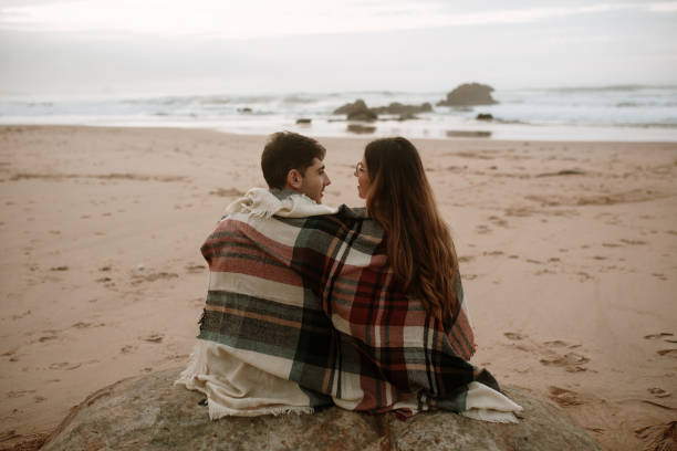 istock Young couple sitting with blanket at beach in autumn 1280377898