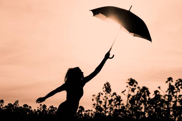 odłączona wolna sylwetka kobieta z parasolem do pomarańczowego nieba - white mid air rain wind zdjęcia i obrazy z banku zdjęć