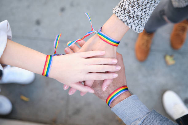 hands of a group of three people with lgbt flag bracelets - gay pride flag fotos imagens e fotografias de stock