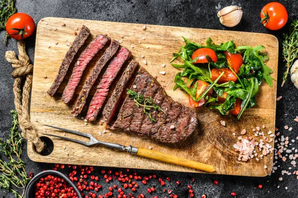 Grilled rump steak with spices on a chopping Board. Barbecue beef. Black background. Top view
