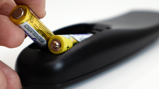 Insert an AAA size battery into the remote control. Installing batteries in a wireless device. A male hand holds a yellow alkaline battery. Replacing the dry camera remote control.