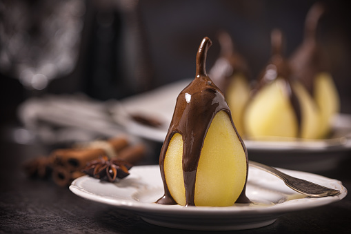 Poached pears glazed with dark chocolate on the dark rustic background