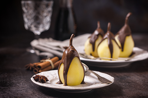 Poached pears glazed with dark chocolate on the dark rustic background