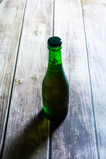 Blond beer on a green bottle closed on a wooden background close up still