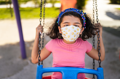 Little girl swinging with her face mask at playground
