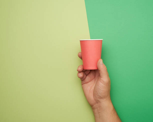 male hand holding red paper disposable cup on green background