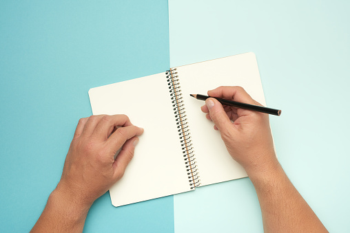 two male hands holding open notepad with empty white sheets on a blue background, top view