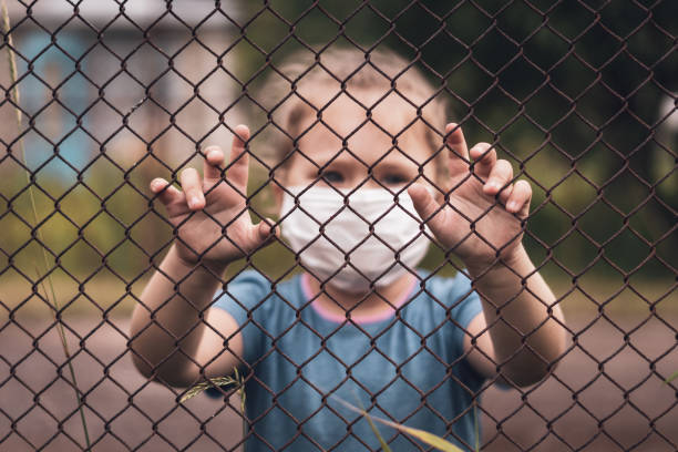A child in a medical mask holds the fence with his hands. Quarantine melancholy and loneliness concepts A child in a medical mask holds the fence with his hands. Quarantine melancholy and loneliness concepts. Phobia stock pictures, royalty-free photos & images