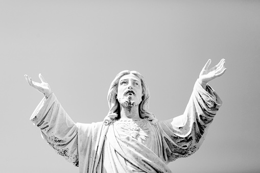 Black and white Old statue of Jesus Christ with hands raised, cemetery build in 1877 Australia, background with copy space, horizontal composition