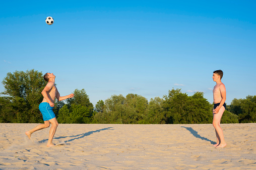 Dad and son play beach soccer on the sand. Summer vacation and healthy lifestyle concept.