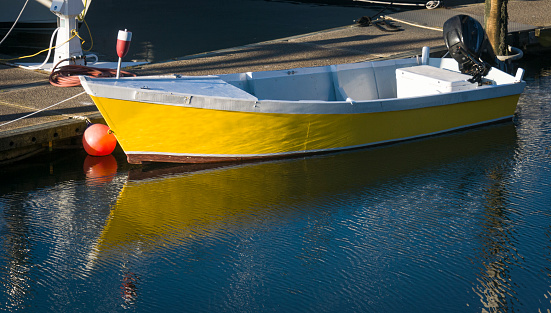 A small bright yellow motor boat is reflected in the waters of the Sandwich Marina on Cape Cod