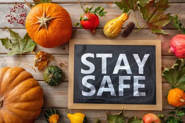 Photo of Stay safe message and thanksgiving pumpkins against wooden background. COVID 19 days