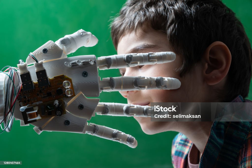 Elementary Schoolboy Touching Robotic Hand Six years old elementary schoolboy meeting humanoid robot. Robotic hand is touching his face gently. The background is green. Shot with a full frame mirrorless camera. Child Stock Photo