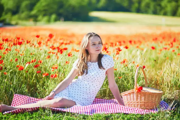 Photo of Woman in white dress having picnic in poppy field on a summer day