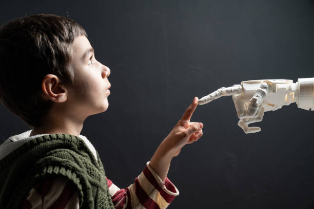 Elementary Schoolboy Touching Robotic Hand Six years old elementary schoolboy meeting humanoid robot. He is touching robotic hand's finger. The background is black. Shot with a full frame mirrorless camera. school science project stock pictures, royalty-free photos & images