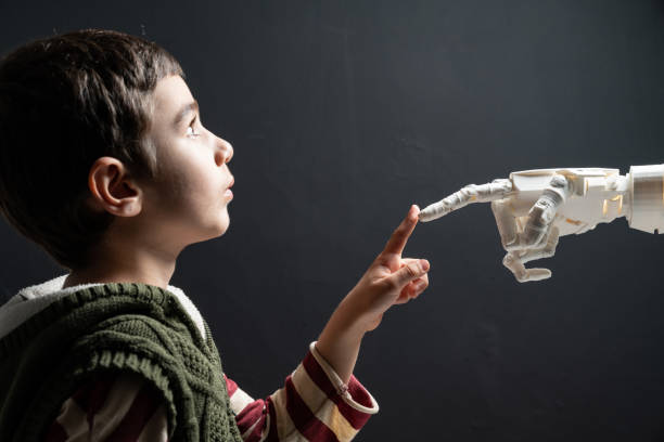 Elementary Schoolboy Touching Robotic Hand Six years old elementary schoolboy meeting humanoid robot. He is touching robotic hand's finger. The background is black. Shot with a full frame mirrorless camera. human finger stock pictures, royalty-free photos & images