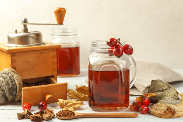 Hot healthy drink made from brewed ground chaga and .hawthorn.In a glass mug decorated with rosehip berries and a vintage coffee grinder. Close up stock photo