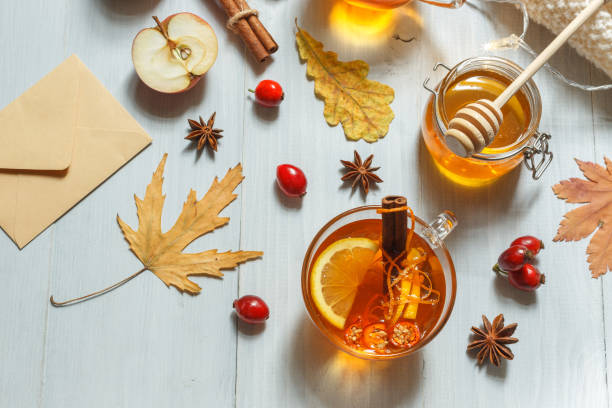 Autumn layout with fragrant hot tea, dry leaves, an envelope and a honey in a jar,autumn or winter hot drink . On a light wooden background with space for text stock photo