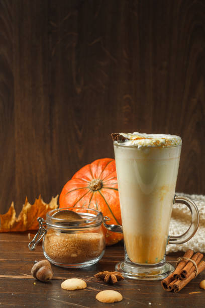 Pumpkin latte in a tall cocktail glass on a dark wooden background, close-up, with a pumpkin and a jar of brown sugar. Copy of the space stock photo