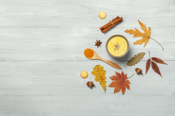 Golden milk with turmeric and spices on a light wooden surface with bright dry autumn leaves. Top view with space stock photo