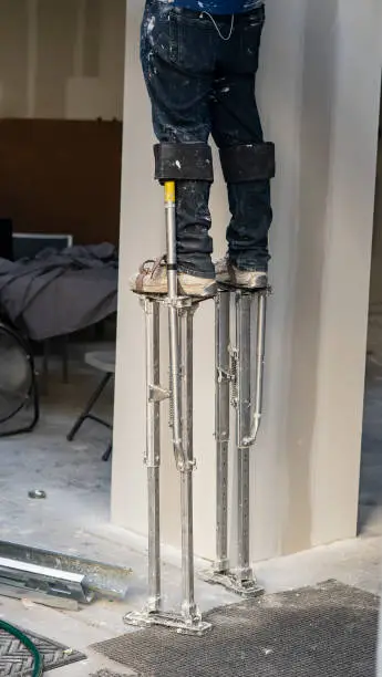 Professional painter using drywall stilts to reach high wall ceiling.