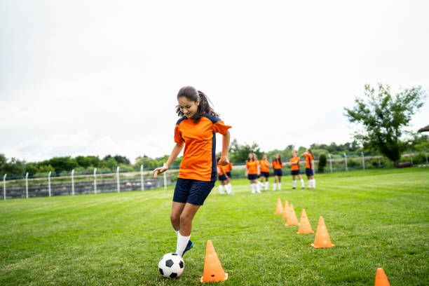 Female soccer player practicing Young female soccer player training on a football field. Young woman practicing her skills, football team standing behind. high school soccer stock pictures, royalty-free photos & images