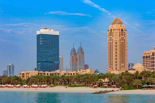 Dubai, United Arab Emirates - It is almost sunset time at Umm Suqueim beach, in Dubai in the United Arab Emirates; the oblique rays of the setting sun hit some of the taller buildings in the background.  The beach is almost deserted at this time of the day. Photo shot from a yacht at an offshore location, late in the afternoon; horizontal format. Copy space. Note to Inspector: the image has more than three building; there are also more than three signs and logos, but no sign is more prominent than the other.