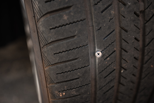 A screw stuck in a car tire puncturing it and making it flat