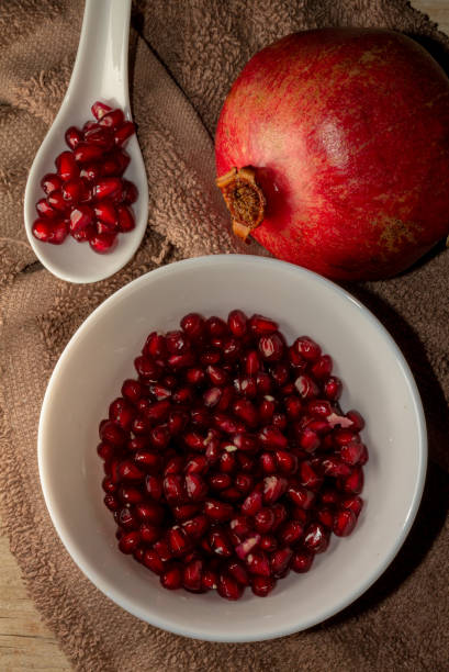 Grains of pomegranate and fruit in a bowl Aerial close up view of grains of pomegranate and fruit in a bowl and a white tasting spoon on the wooden table and brown cloth.  Natural vitamin supplement for a healthy diet pomegranate stock pictures, royalty-free photos & images