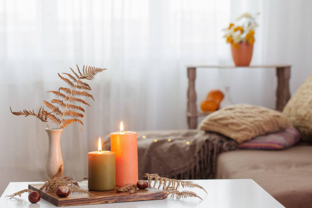 burning candles with autumn decor on white table at home stock photo