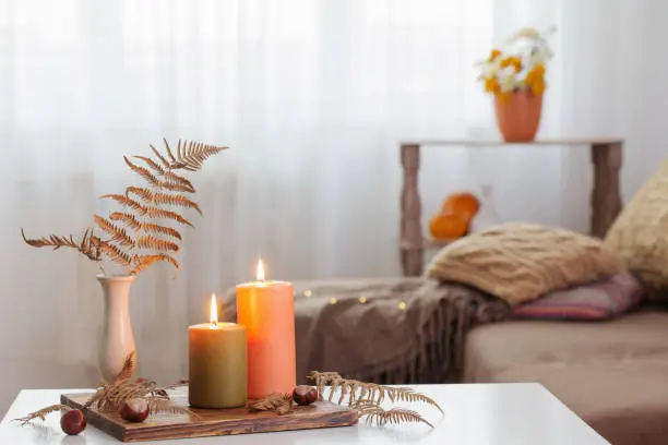 Photo of burning candles with autumn decor on white table at home