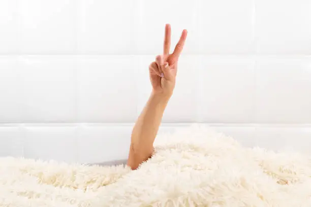 Photo of Female hand show a v sign in a white bed, a wonderful start to a new day, good morning. copy space