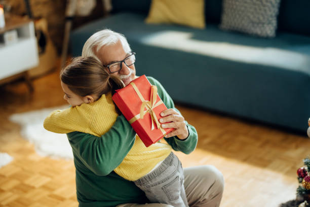 wdzięczna dziewczynka obejmująca swojego dziadka podczas przyjmowania prezentu bożonarodzeniowego w domu. - granddaughter feelings behavior family zdjęcia i obrazy z banku zdjęć