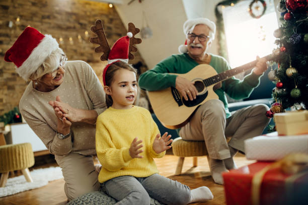 自宅でクリスマスに楽しんでいる孫娘と喜びの祖父母。 - traditional song ストックフォトと画像