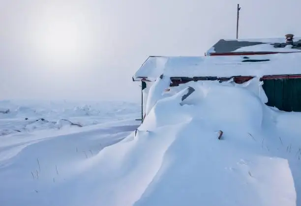 As the sun rises in the morning, a steep pile of fresh snow covers a house wall, reaching the roof, after an Arctic blizzard in the Canadian north.