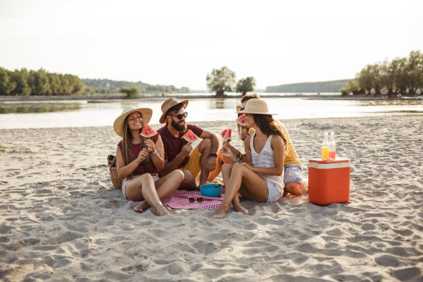 amigos disfrutando de sandía en un picnic en la playa - number of people riverbank beach river fotografías e imágenes de stock